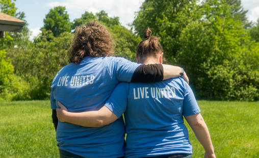 Two women walk with their arms on each other's shoulders wearing t-shirts that say Live United